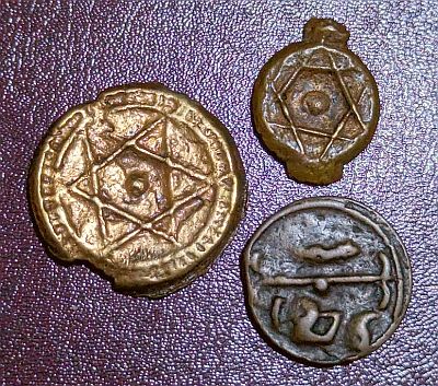 1, 2, and 4 Falus coins, each larger in size. The 4 falus coin has a striped ring around the Seal of Solomon, and also has a small piece missing where too much of the sprue was cut off. The 2 Falus is showing the obverse side with the year (1276 - 1860) and part of the mintmark of Fes mint in Arabic), divided by a line with a dot in the centre.