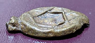 Side view of Moroccan falus coin with indentation and raised lines of the Seal of Solomon visible and the edge protrusions from the tree.