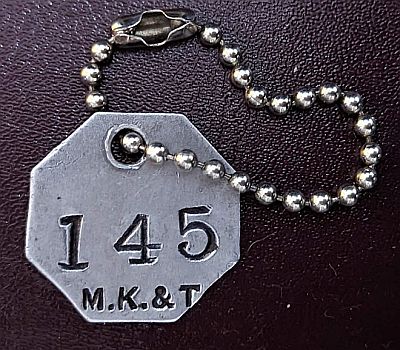 M.K.&T. octagonal aluminium check. Hole near top with chain. Numbered 145.