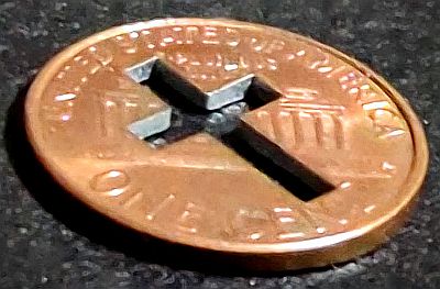 Lincoln penny with cross cut out, on an angle so the cutout shows the zinc center of the coin.