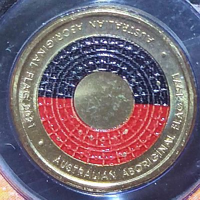 The Australian Aboriginal Flag design is represented on the coin with the black and red fields printed over a relief pattern of miniature flags. The centre of the coin has been left print-free allowing the gold of the coin’s alloy to shine through as a unique representation of the central yellow sun motif. Script: Latin Lettering: AUSTRALIAN ABORIGINAL FLAG 1971 (Upside Down) AUSTRALIAN ABORIGINAL FLAG 2021 Designer: H. Thomas