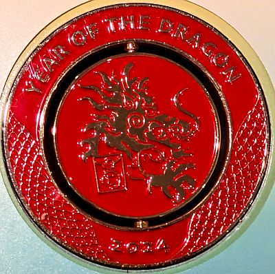 Reverse of the medallion showing YEAR OF THE DRAGON aabove in the fixed part, and 2024 at the bottom, both in gold on a red background. In the centre movable part, is a dragon's head facing right with the dragon symbol below, all in gold on a red background.. There is a fine "dragon skin" type design on the outer part between the title and year