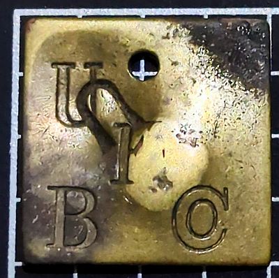 United Fruit Company tally. Square with a hole in the top and U F Co (with the o inside the C) diagonally downwards, and B in the bottom left. There is a U which has been ahnd stamped afterwards, almost upside down between the U and F of the company letters.