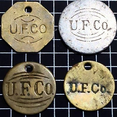 Four United Fruit Co tallies, each with U.F.Co. across the middle and three with rounded lines above and below. The top-right one is aluminium with no hole. The rest are bronze with holes and the top-left is octagonal.