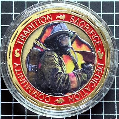 The reverse features a modern firefighter, wearing breathing apparatus and holding an axe.  Behind the firefighter is a "Florian Cross" full of fire.  Around the edge are some of the qualities valued in firefighters: Sacrifice, Dedication, Community and Tradition.