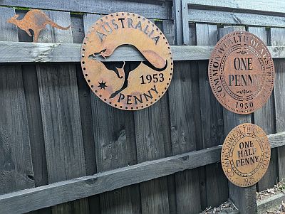 Metal signs with representations of a 1953 Penny reverse, a 1930 (old style) penny reverse and 1925 half penny reverse.  There is also a small kangaroo looking like it jumped out of the penny.